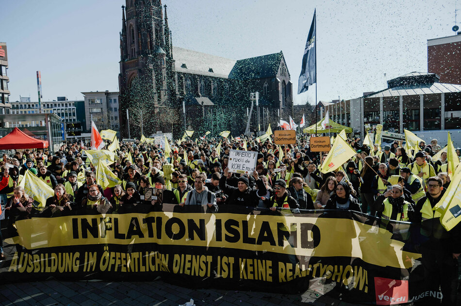 Hunderte Streikende vor einer großen Kirche halten ein Banner hoch auf dem steht: Inflation Island - Ausbildung im öffentlichen Dienst ist keine Realityshow